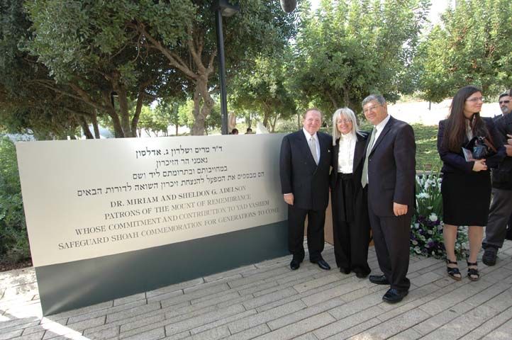 בני הזוג אדלסון ויו"ר הנהלת יד ושם אבנר שלו ניצבים ליד שלט ההוקרה על תרומתם להנצחת זיכרון השואה 