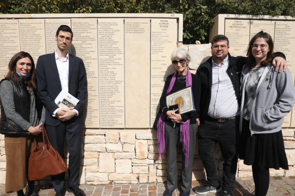ליז דולב עם משפחת הניצול לצד שמו של אביה על הקיר בגן חסידי אומות העולם ביד ושם