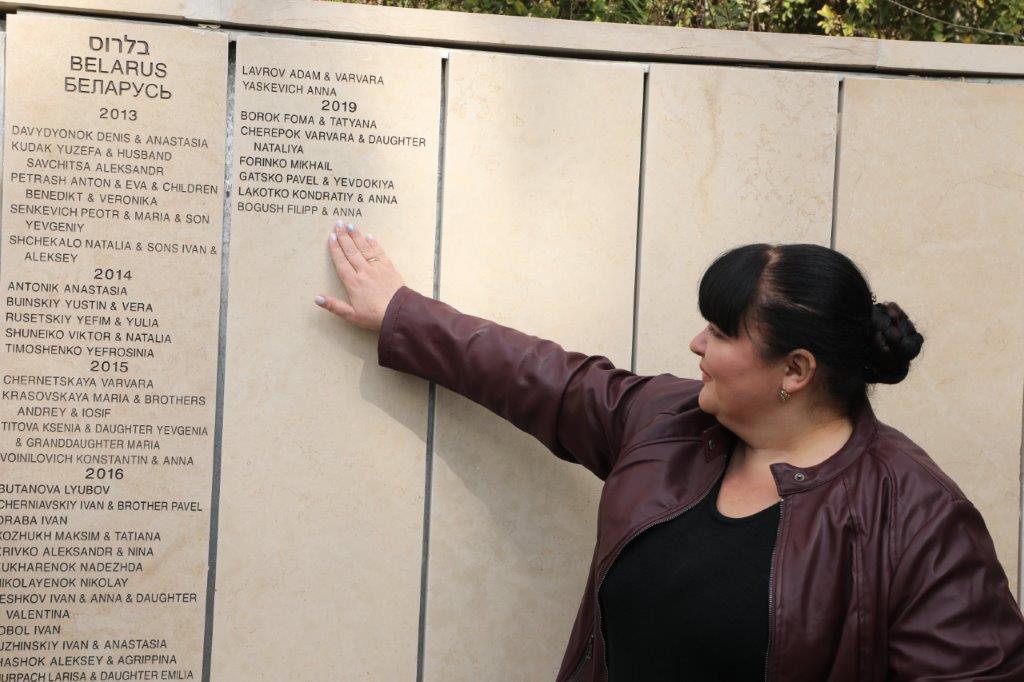 ילנה קימברובסקי מצביעה על שמות סבתה וסבה חסידי אומות העולם אנה ופילפ בוגוש החרוטים  על הקיר בגן חסידי אומות העולם ביד ושם
