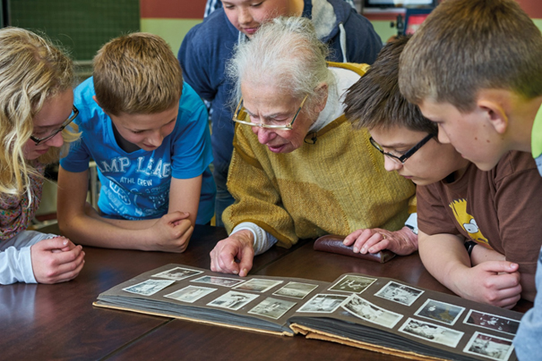Helga Becker-Leeser mit Schülern, ihr Familien-Fotoalbum zeigend. 