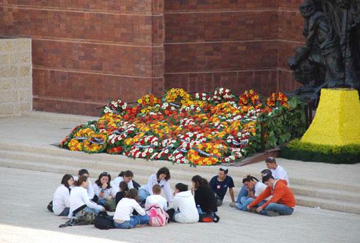 תלמידים יושבים ברחבת כיכר גטו ורשה במסגרת ביקורם ביד ושם