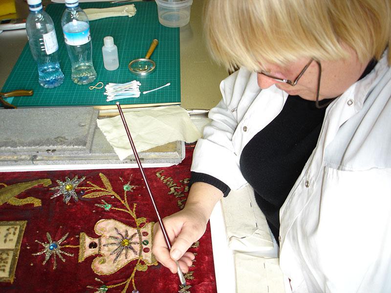 אלכסנדרה בורובק, רסטורטורית באוסף החפצים, במהלך עבודות שימור של מעיל לספר תורה מסלוניקי, לקראת פתיחת התצוגה בבית הכנסת ביד ושם, יוני 2005
