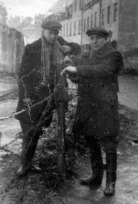 Jan Kostanski (left) and Ajzyk Wierzbicki pose on opposite sides of the barbed wire fence on Krochmalna Street. (United States Holocaust Memorial Museum)