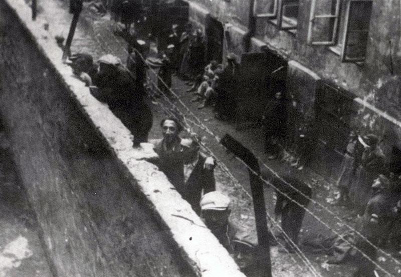 אייזיק ויעקב וייז'ביצקי עומדים על סולם הנשען על חומת הגטו ומשקיפים על ככר מירובסקי 