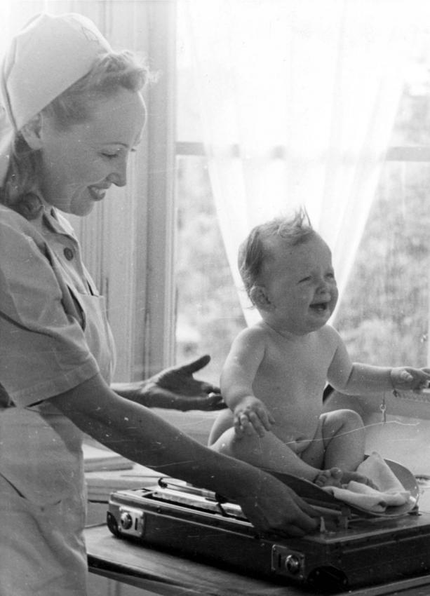 An infant being weighed by a nurse in a DP camp, Munich