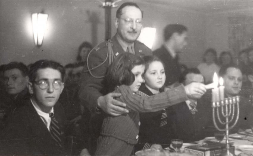 הרב הראשי של צבא ארצות הברית באירופה, גולדמן, מדליק נר שלישי של חנוכה עם ילדות במחנה העקורים פירסטנפלדברוק (Fuerstenfeldbruck), גרמניה, 1945