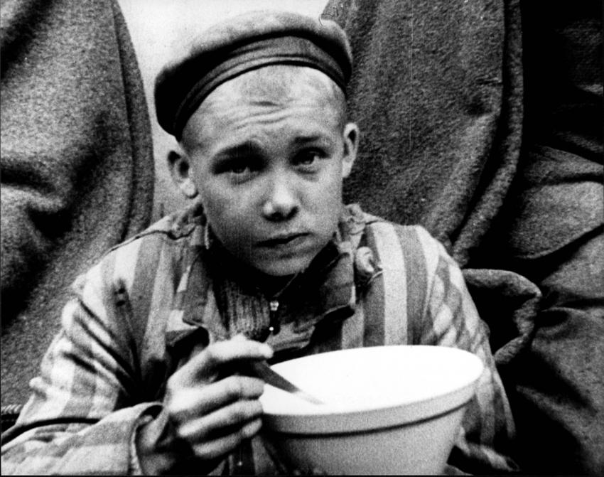 נער במדי אסיר אוכל את ארוחתו הראשונה, בזמן השחרור, מחנה דכאו, גרמניה