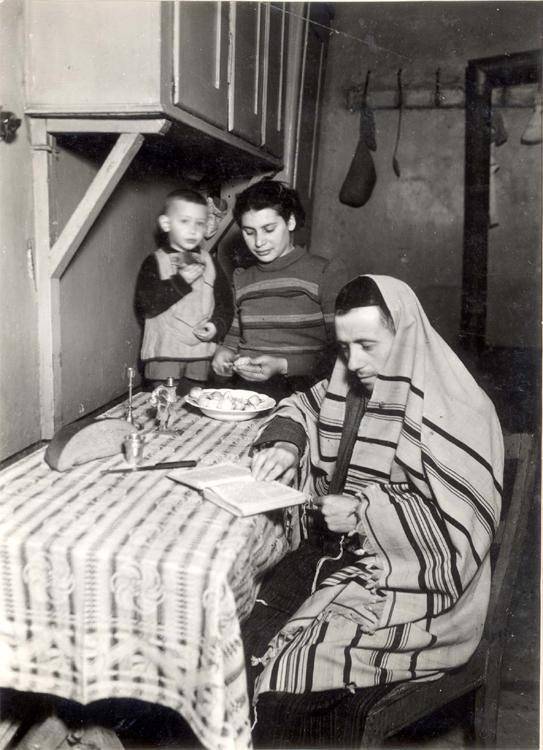 Varsovia, Polonia, un hombre rezando con un mantón de rezo junto a una mujer y un niño, en lo que había sido una sinagoga