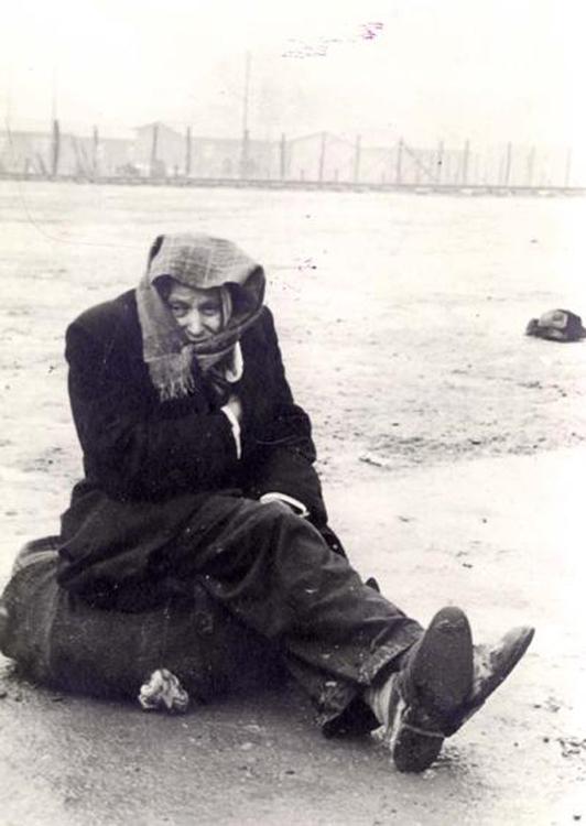 A survivor sits on a bundle of possessions after liberation, Dachau, Germany