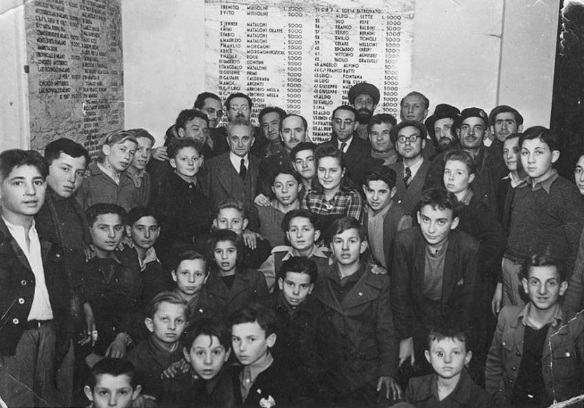 The Selvino children and their counselors in the entrance hall of the “Sciesopoli” building, in front of the list of donors headed by Benito Mussolini.