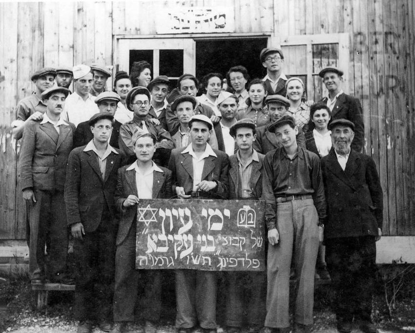 Group of refugees holding a sign that reads: “Bnei Akiva Kibbutz study days. Feldafing, Germany, 1945-46&quot;