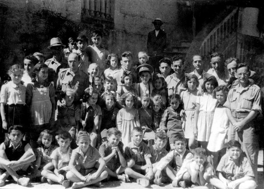Soldiers from Eretz Israel serving in the British Army with children at a school in the Santa Maria di Bagni refugee camp in Italy, a camp housing Jews and non-Jews.
