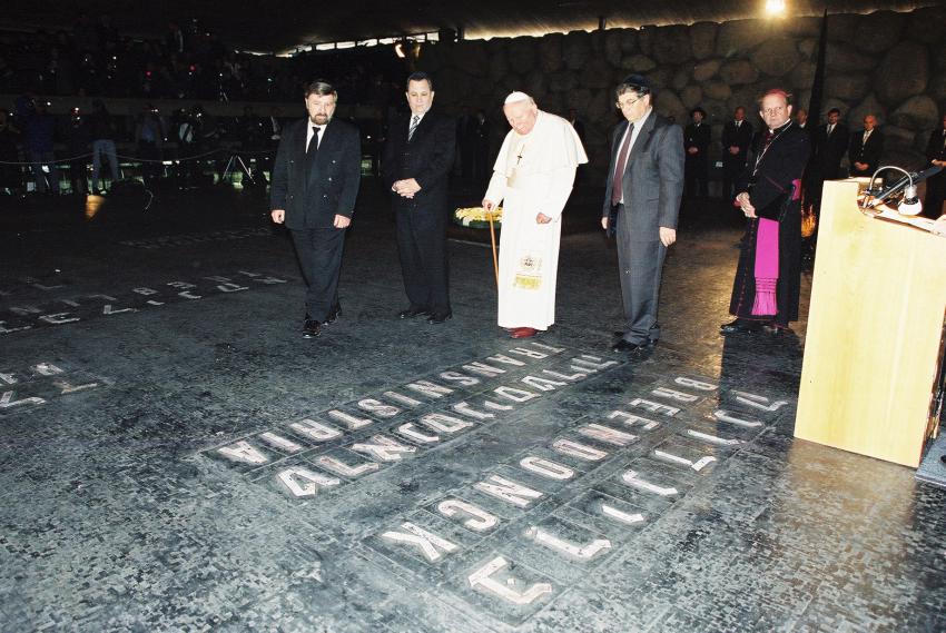 האפיפיור יוחנן פאולוס השני בוחן את אחד משמות אתרי ההשמדה המופיעים על רצפת אוהל יזכור