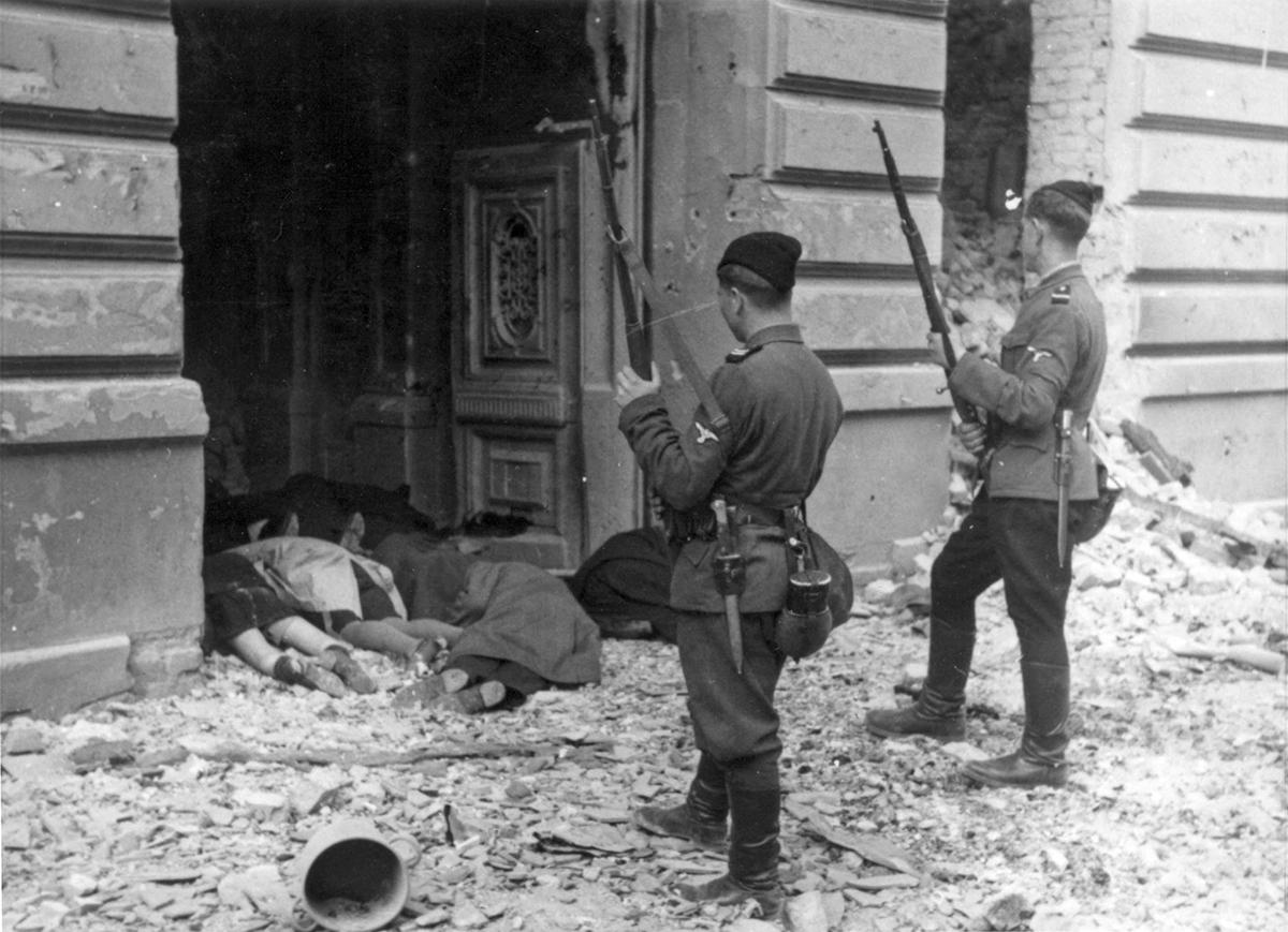 Two members of a Ukrainian militia unit stand opposite the corpses of Jews killed during the Warsaw Ghetto Uprising