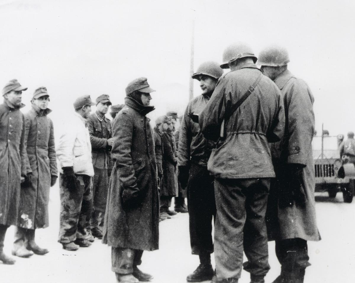 Robert Brand interrogando a un prisionero de guerra alemán (Brand, tercero desde la derecha, de pie frente al prisionero)