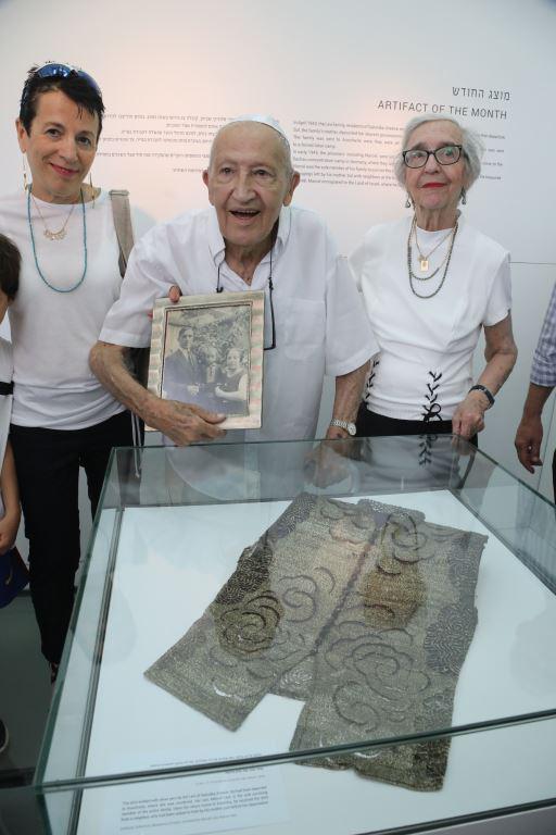 מרסל לוי מחזיק תמונה של משפחתו שנרצחה בשואה ולידו אשתו רחל לוי ובתו נורית פרחי