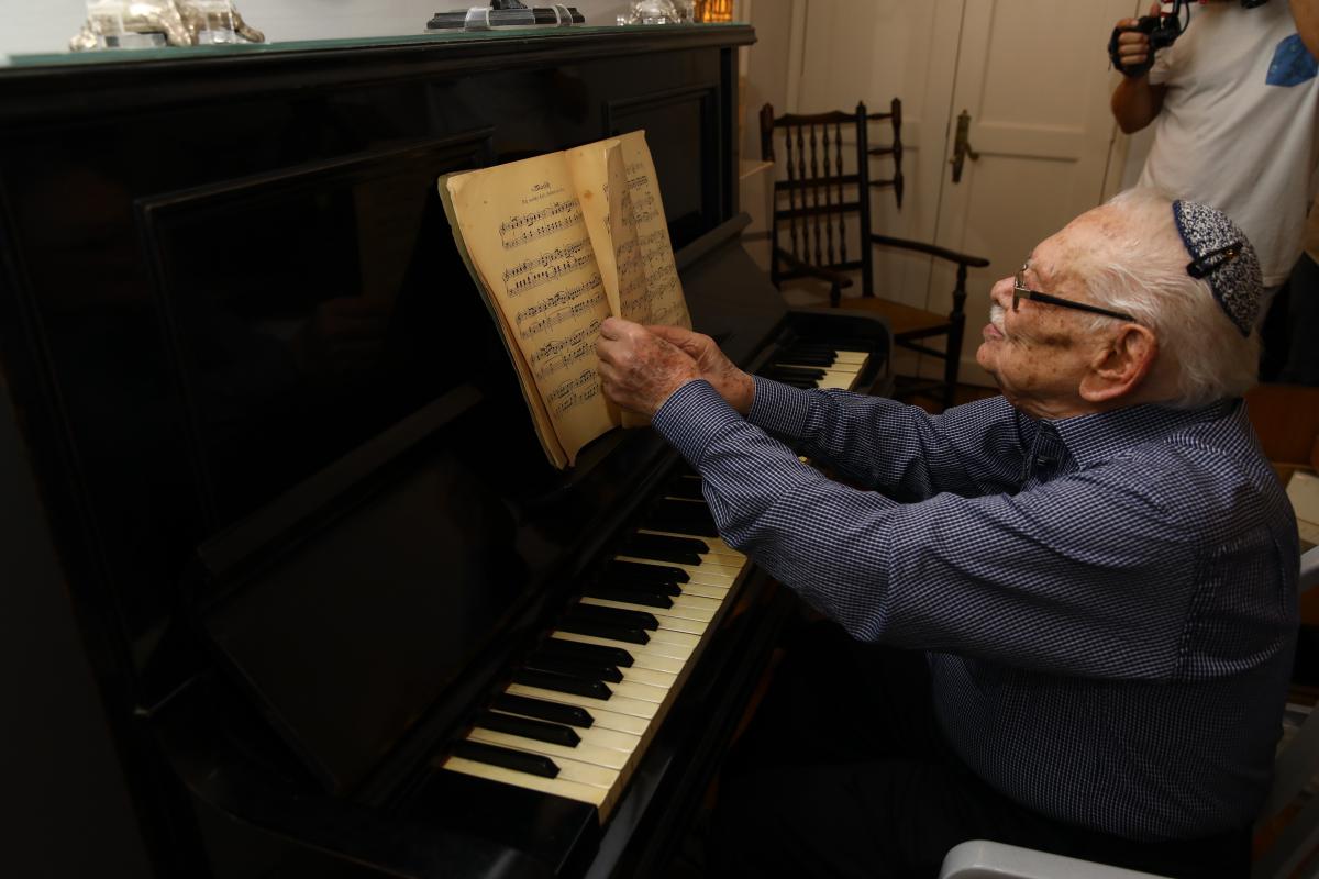 Holocaust survivor Shlomo Margulies sitting at his precious piano which is now on display at Yad Vashem's Holocaust History Museum 