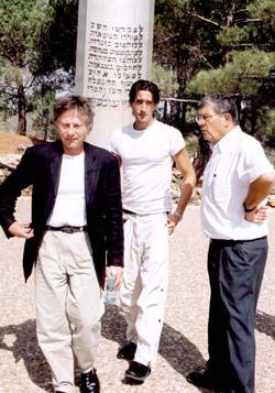 Roman Polanski (left in black jacket) accompanied by Avner Shalev (right) and Adrian Brody (center) as they stand in front of the Pillar of Heroism