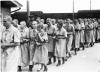 Photo n°25 : Détenues juives marchant dans le camp des femmes dans l'uniforme des détenus. A gauche, un SS les regarde.