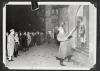 Una multitud de transeúntes, incluidos civiles, hombres de las SS y SA, observan a un miembro de las SS destrozando un negocio de propiedad judía durante la Kristallnacht, Núremberg, 1938