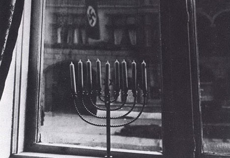 Fotografie, aufgenommen 1931 von Rahel Posner in ihrer Wohnung in Kiel: Ihr entzündeter Chanukkah-Leuchter mit der Nazifahne im Hintergrund