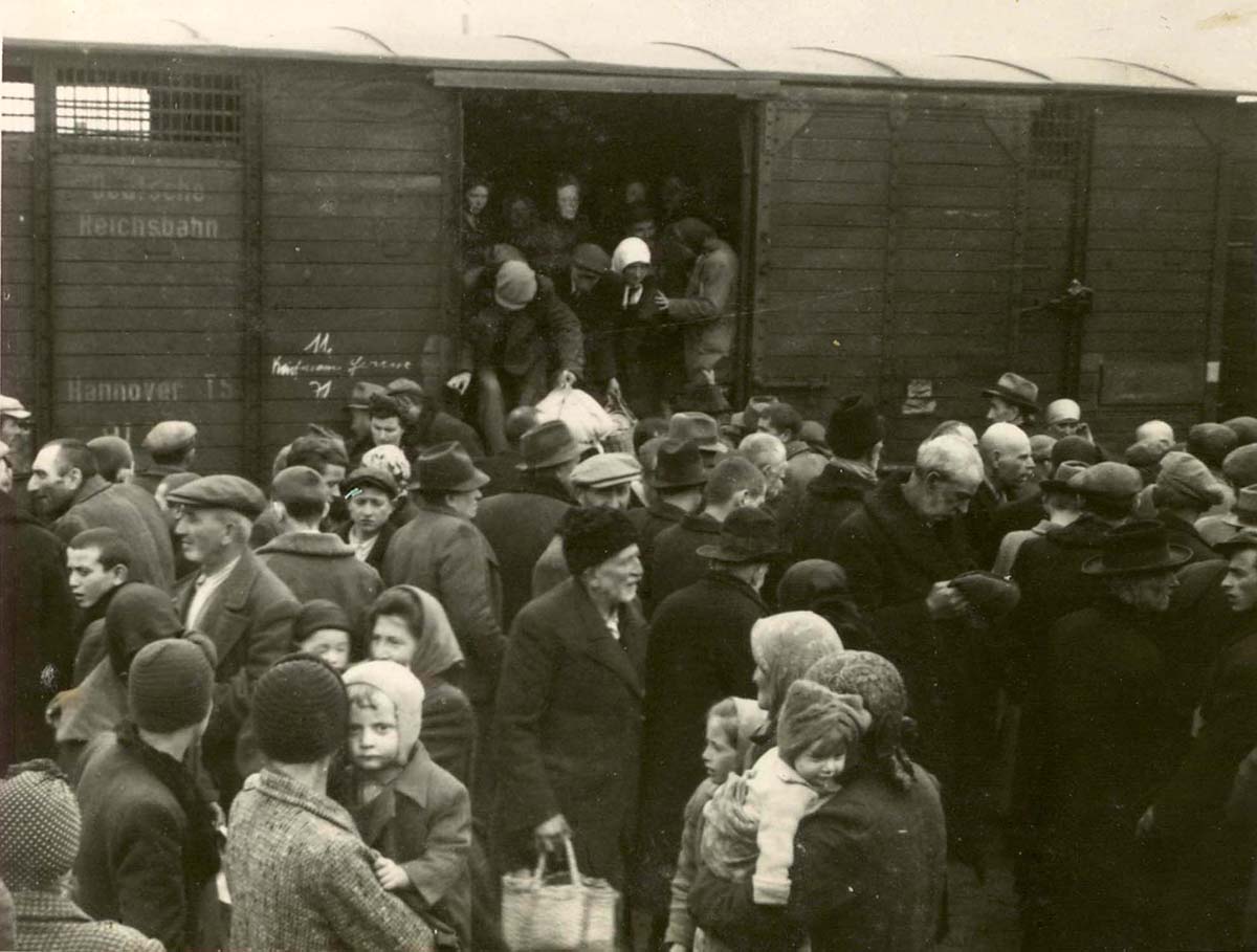 Since the railroad car has no convenient steps, the old Jews have to be assisted in disembarking. The words written on the side of the train are "Deutsche Reichsbahn" ("German State Railway")