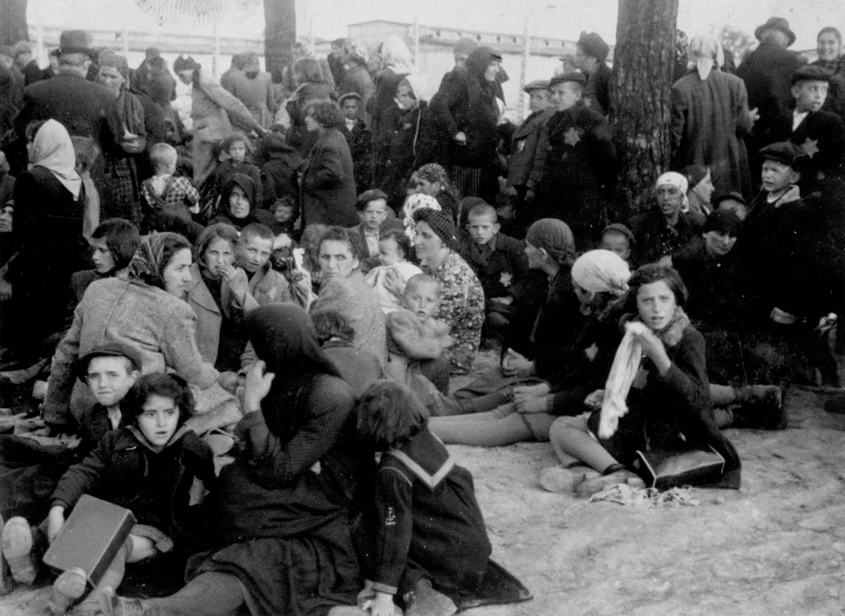 Derniers instants que les Juifs passent ensemble sereinement, avant d'être poussés vers les chambres à gaz et assassinés. Au fond : les baraques de la zone « Kanada ».