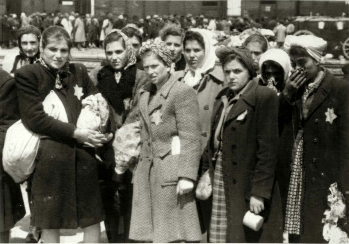 The Jewish women, now prisoners, have been permitted to carry small packages. First row, from left to right: Lili ("Bobo") Yakobovics of Tacovo (survived the Holocaust), Rozi Bittman, Rozi Grever (survived the Holocaust). Second row: Ester Klein, Sima Müller, Mariska Müller