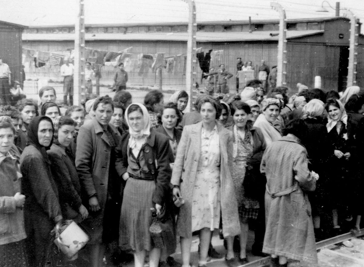 Jüdische Frauen in Birkenau auf dem Weg zur „Sauna& (ein Duschraum). Die Männer hinter dem elektrisch geladenen Stacheldraht sind ebenfalls Häftlinge in Birkenau