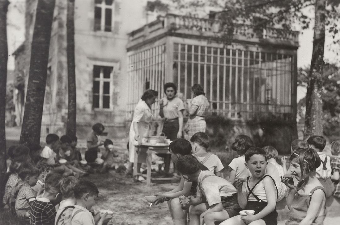 Herbert Odenheimer (Ehud Loeb) (front, with the crossed-over shoulder straps) at the children's home in Chabannes, 1941. In 2007, Ehud Loeb visited the "Memoriale de la Shoah" in Paris and viewed an exhibition  about children's homes established by the OSE (Oeuvre de Secours aux Enfants), which worked to rescue children in France.  Loeb identified himself amongst his friends and the staff in this photograph.