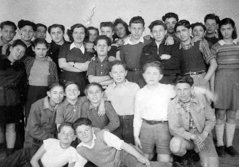 המורה לעברית חנה אייזנשטיין (בידיים שלובות) מוקפת בתלמידיה בכפר הילדים "אילניה". אפלדורן, הולנד 1947