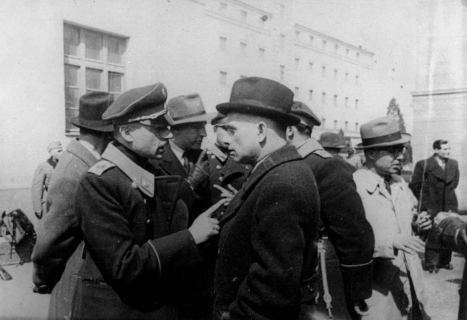 The Commissar for Jewish Affairs Alexander Belev (third from left) speaking to his assistants during a visit to the place where the Jews were concentrated, the “Monopol” tobacco factory storerooms, seen in the background, Skopje, March 1943