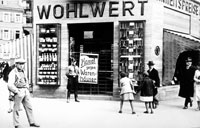 Würzburg on  "Boycott Day ", 1 April 1933. An SS man stands in front of a Jewish business, which is blocked by a sign calling shoppers to boycott the store. The sign reads:  "Fight the [Jewish] Department Stores ".