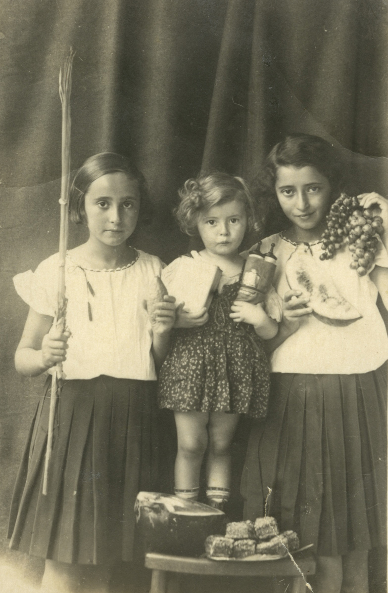 Sisters Donia (right) and Esther Sorger on the Succot festival and their toddler sister Sonia holding a miniature Torah scroll