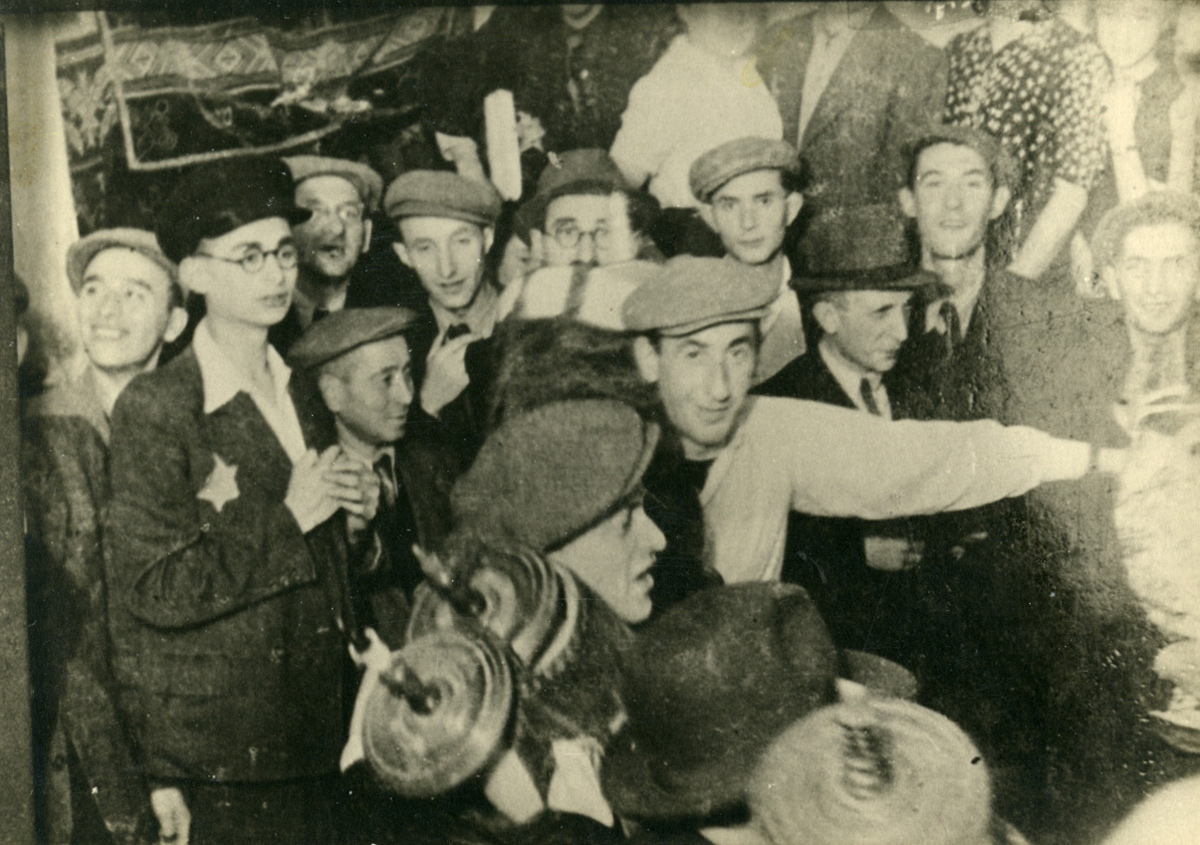 אהרון יעקבסון (במרכז, בחולצה בהירה) וחבריו ל"חזית הנוער הציוני" רוקדים עם ספר תורה בשמחת תורה. גטו לודז', אוקטובר 1943