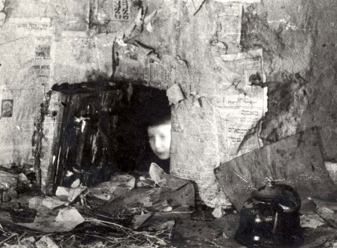 מוישלע קאפאנסקי זוחל החוצה ממחבואו, דרך חור בקיר. וילנה, ליטא, 1944 (לאחר השחרור)
