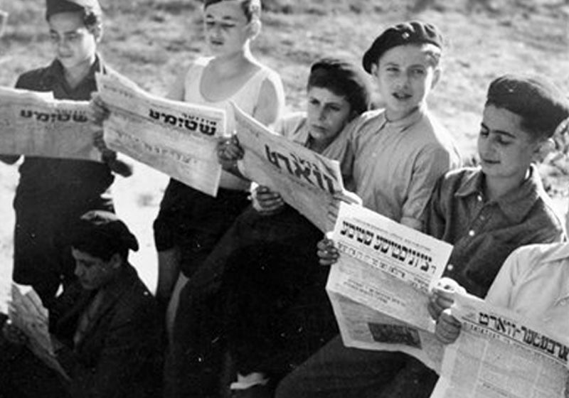 Des "enfants de Buchenwald" à la maison d'enfants d'Ambloy, en train de lire des journaux en Yiddish. France, 1945