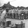 Distribution of food to prisoners in Flossenbürg. The prisoners, who were assigned to  the granite quarry, stood to attention before receiving a portion of food from the kapo. Germany, 1944.